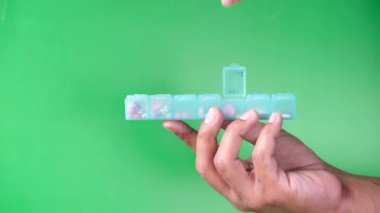 Adamın elleri yeşil arka planda ilaç kutusundan ilaç alıyor. 