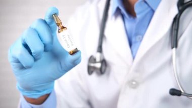 Ellerinde cam ampul aşısı tutan lateks eldivenler var. 