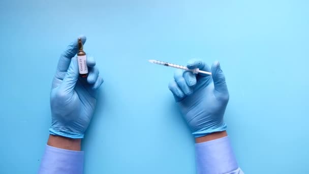 Mână în mănuși din latex care dețin vaccin fiolă de sticlă și o seringă pe albastru — Videoclip de stoc