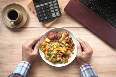  Genç adam dizüstü bilgisayarla çalışırken taze salata yiyor. 