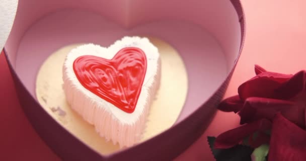 Vue du dessus du gâteau en forme de coeur, de la boîte cadeau et de la fleur de rose sur fond rouge — Video