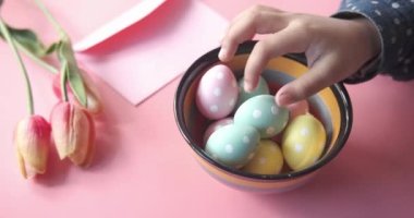 Çocuk eli ile paskalya konsepti pembe arka planda renkli yumurta seçer.