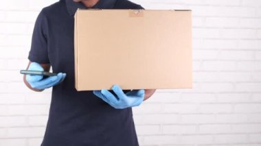 Teslimatçı, elinde akıllı telefon ve kart kutusu tutan lateks eldivenler getirdi.,