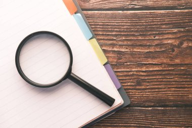 Masanın üzerinde açık kitap ve büyüteç.