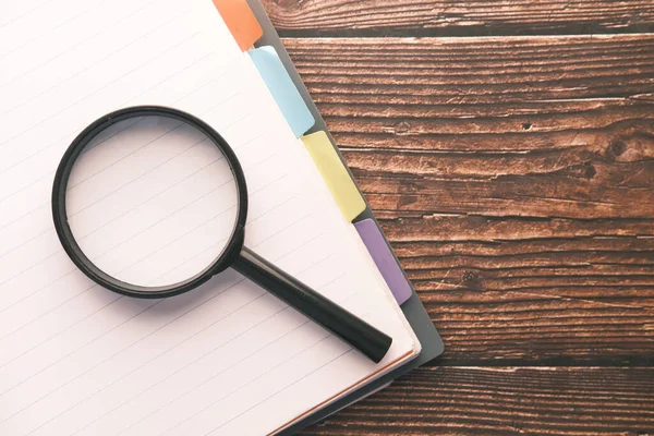 Masanın üzerinde açık kitap ve büyüteç.