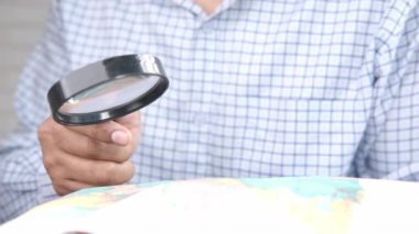 Genç adam haritada bir şeye bakarken büyüteç kullanıyor. 