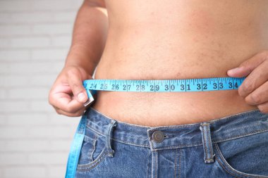 Genç adam kemerini bir mezura ile ölçüyor. Yaklaş..