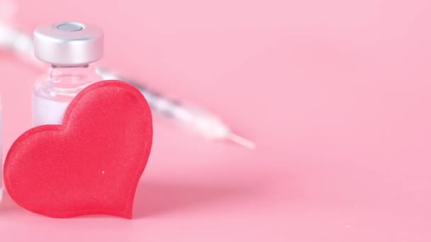 Close up da vacina contra o coronavírus, seringa e coração vermelho sobre fundo rosa — Vídeo de Stock