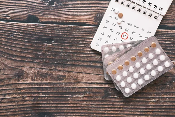 top view of birth control pills and a calendar on wooden background,