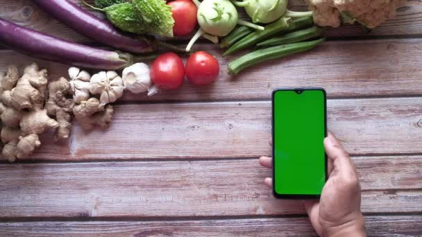 Verduras frescas y sosteniendo el teléfono del mercado con pantalla verde en la mesa — Vídeo de stock