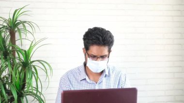  Laptop üzerinde çalışan maskeli genç bir işçi. 