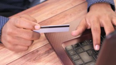 Adamın elleri kredi kartını tutuyor ve internetten bilgisayar alışverişi yapıyor. 