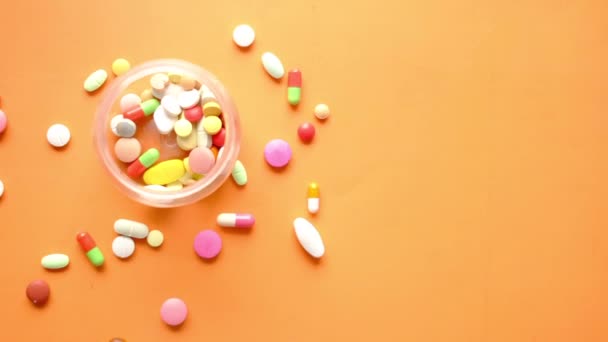 Close-up de muitas pílulas coloridas e cápsulas derramando no fundo laranja — Vídeo de Stock