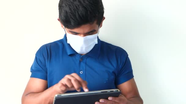 Человек в защитной маске с помощью цифровой таблетки на белом фоне — стоковое видео