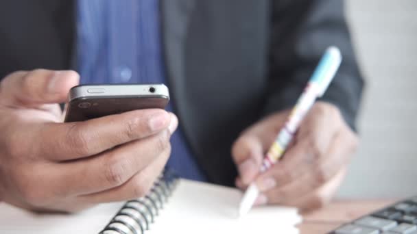 Primer plano de la mano del hombre de negocios utilizando el teléfono inteligente y la escritura en el bloc de notas — Vídeo de stock