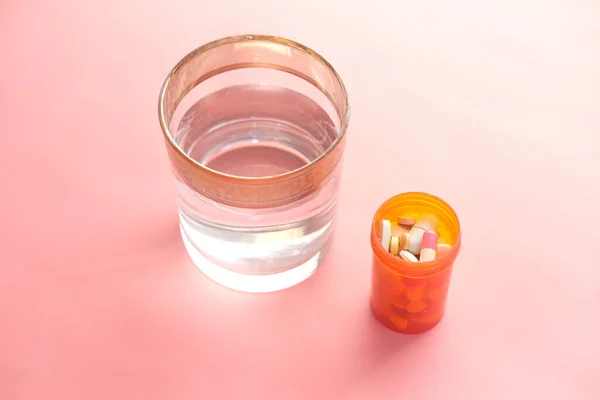 medical pill container and glass of water on pink