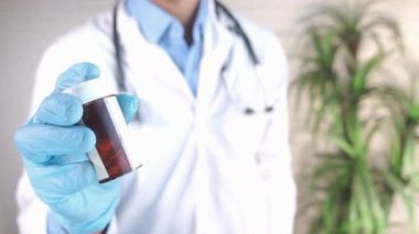 Doktor, koruyucu eldivenler içinde, elinde hap kutusu tutuyor. 