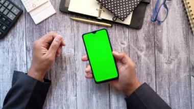 Ofis masasında akıllı telefon kullanan bir adamın üst görüntüsü. 