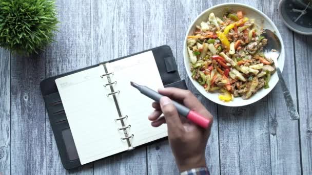 Hand skriva text diet på plan på anteckningsblock med färska kokta sallad på plattan — Stockvideo
