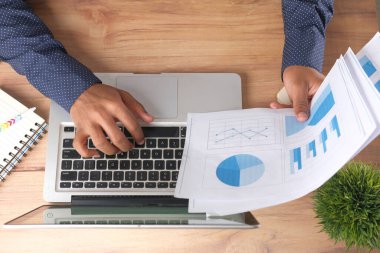 Kalem çizelgesini kağıt üzerinde analiz eden ve dizüstü bilgisayar kullanan bir adam. 