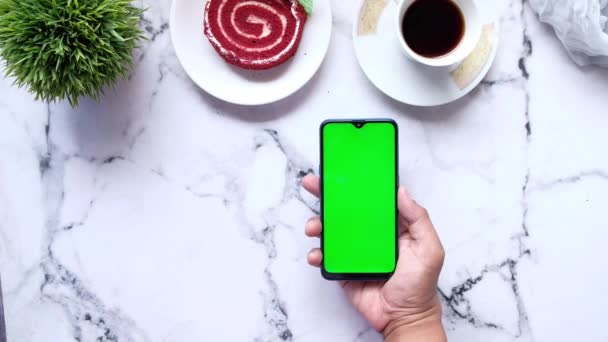 Hånd holder smart telefon med te og en kage på fliser baggrund – Stock-video