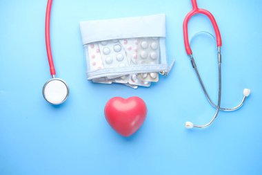 Kalp şeklindeki sembol, su toplayan haplar ve mavi arka planda steteskop. 