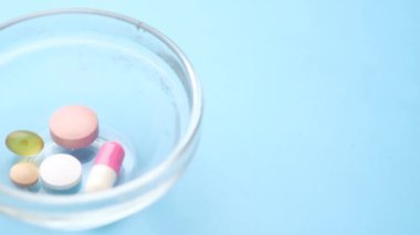 Tıbbi hapları ve kapsülleri mavi arka plandaki küçük bir konteynıra kapatın. 