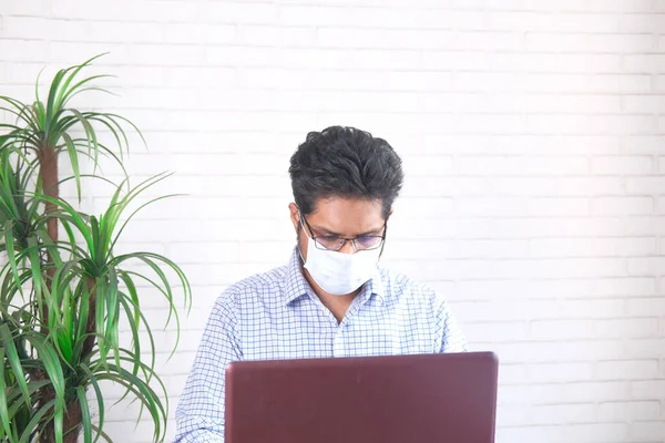 Yüz maskeli bir iş adamı dizüstü bilgisayarla çalışıyor. — Stok fotoğraf