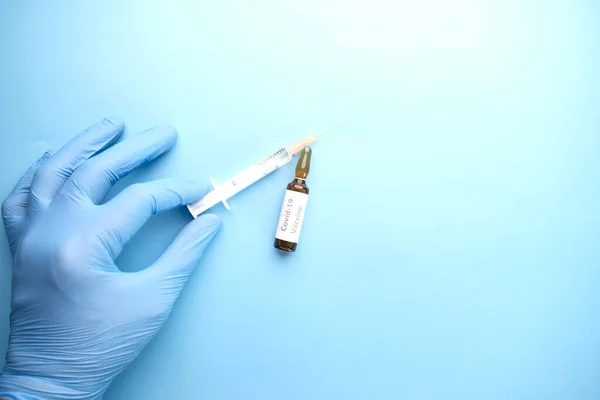 Mano en guantes de látex, vacuna contra ampollas de vidrio y jeringa sobre la mesa — Foto de Stock