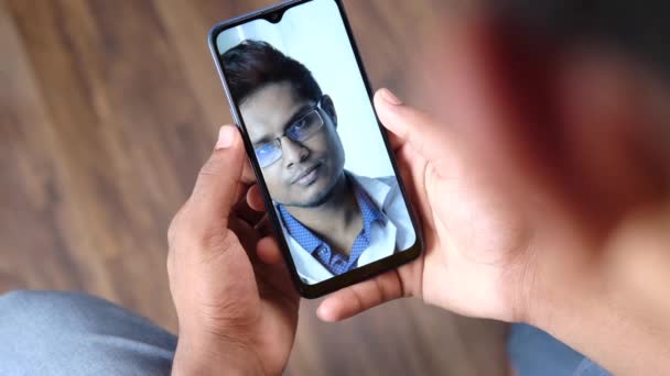 Vista trasera del joven que toma consulta en línea con el médico en el teléfono inteligente — Vídeos de Stock