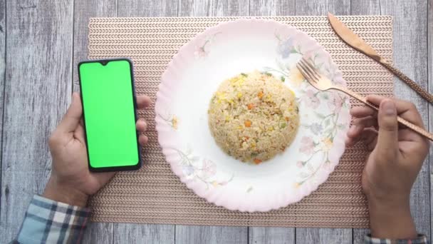 Young man hand holding smart phone and eating cooked rice — Stock Video