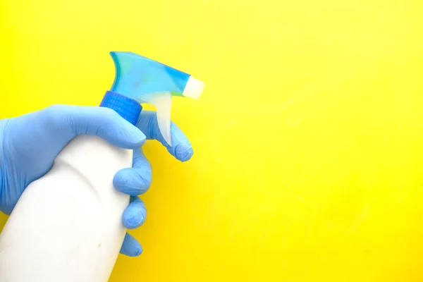 Mano en guantes de goma azul sosteniendo la botella de aerosol sobre fondo amarillo —  Fotos de Stock