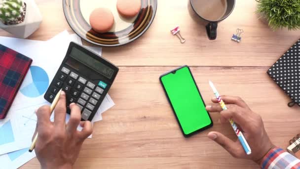 Hand mit Smartphone und Taschenrechner auf dem Tisch, von oben nach unten — Stockvideo