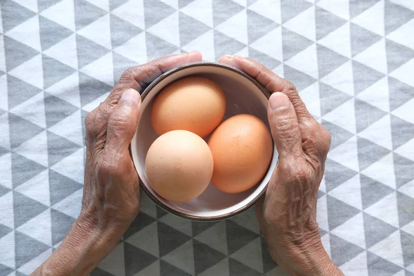 Senior femmes main tenant un bol d'œufs sur la table — Photo