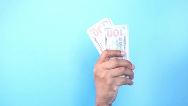 Рука держит 100 долларов наличными на синем фоне — стоковое видео