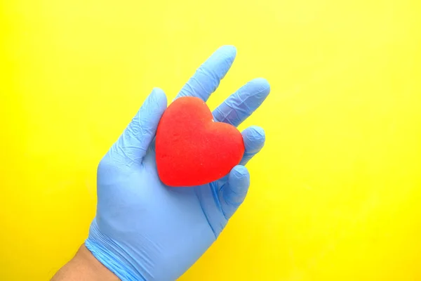 Man hand in protective gloves holding red heart on yellow background Stock Picture