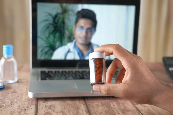 Online διαβούλευση με το γιατρό στο φορητό υπολογιστή και κρατώντας ένα δοχείο ιατρικών χαπιών — Φωτογραφία Αρχείου