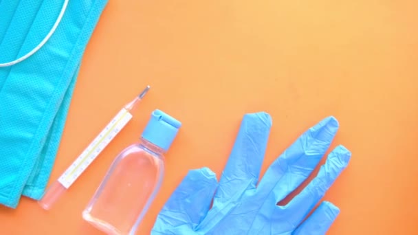 Mascarillas quirúrgicas, termómetro y desinfectante de manos sobre fondo naranja — Vídeo de stock