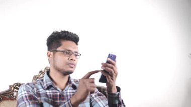Kanepede oturan üzgün genç adam akıllı telefon kullanıyor..