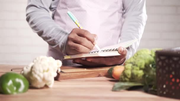 Young man writing on notepad on kitchen table — Stock Video