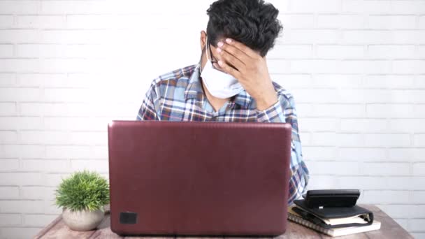 En ung asiatisk man med skyddande mask i ansiktet mår illa och arbetar på laptop — Stockvideo