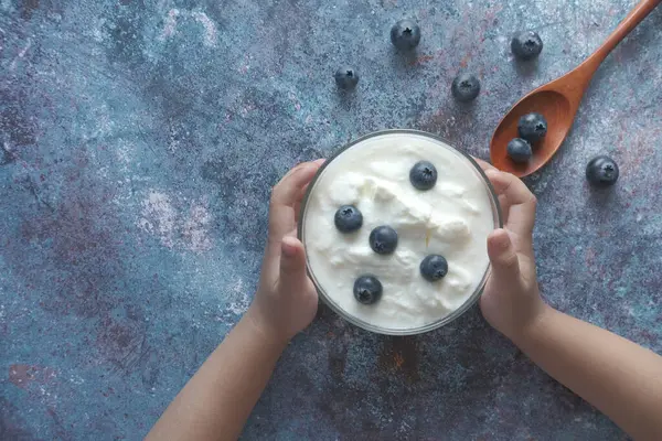 Kinderhand hält eine Schale mit frischem Joghurt mit blauen Beeren — Stockfoto