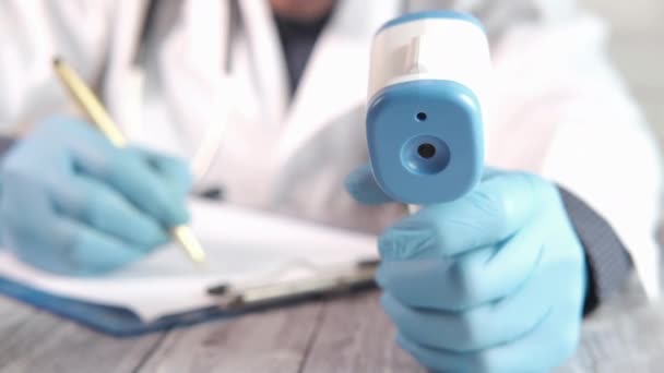 Medico mano tenendo termometro a infrarossi e scrittura su carta — Video Stock