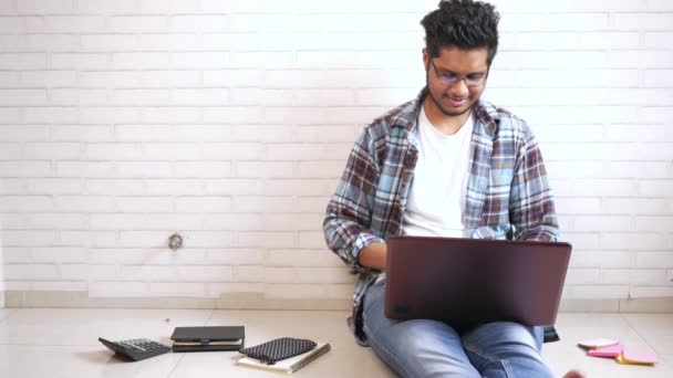 Mladý muž v ležérní šaty sedí na podlaze pracuje na notebooku — Stock video