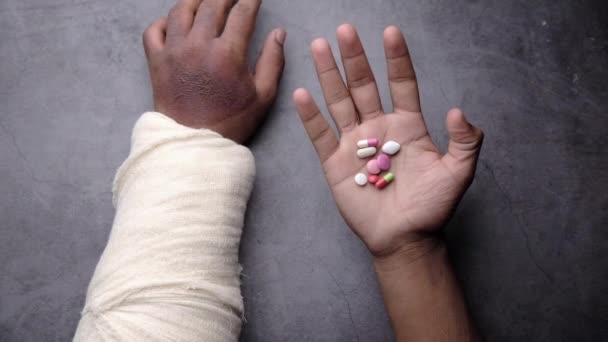 Mano dolorosa lesionada con vendaje y píldoras médicas en la mano — Vídeos de Stock