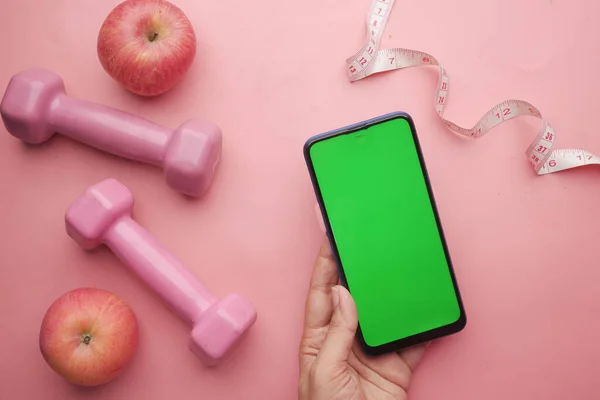 Mulheres mão segurando telefone inteligente com s haltere e maçã em rosa — Fotografia de Stock