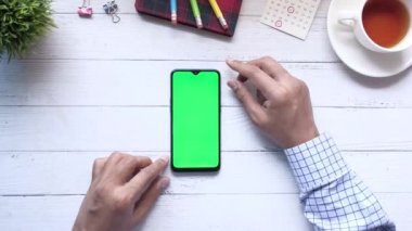 Ofis masasında akıllı telefon kullanan bir adamın üst görüntüsü. 