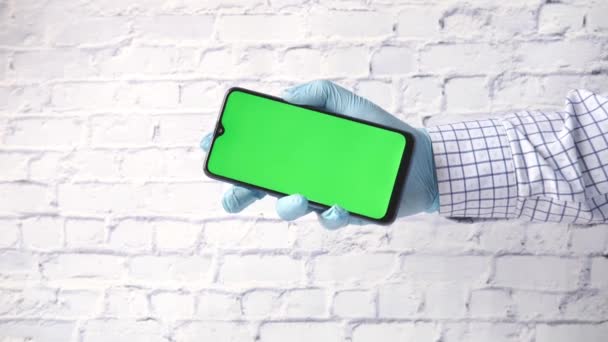 Hand in Latex-Handschuhe mit Smartphone und grünem Bildschirm — Stockvideo
