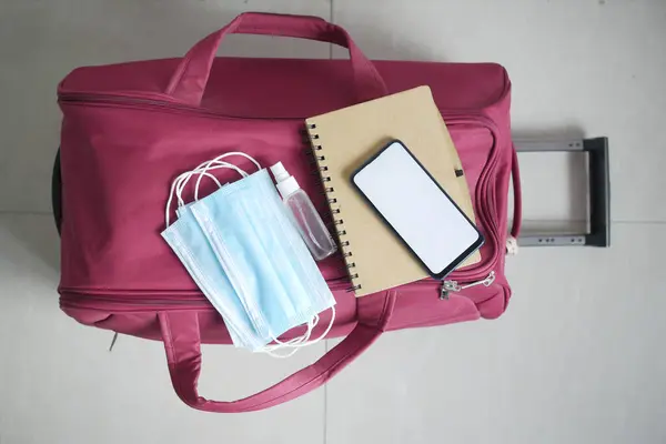 Smartphone, Reisepass, Händedesinfektionsmittel und Mundschutz auf dem Koffer am Boden — Stockfoto