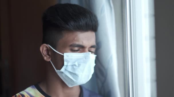 Um jovem com máscara protetora olhando pela janela — Vídeo de Stock